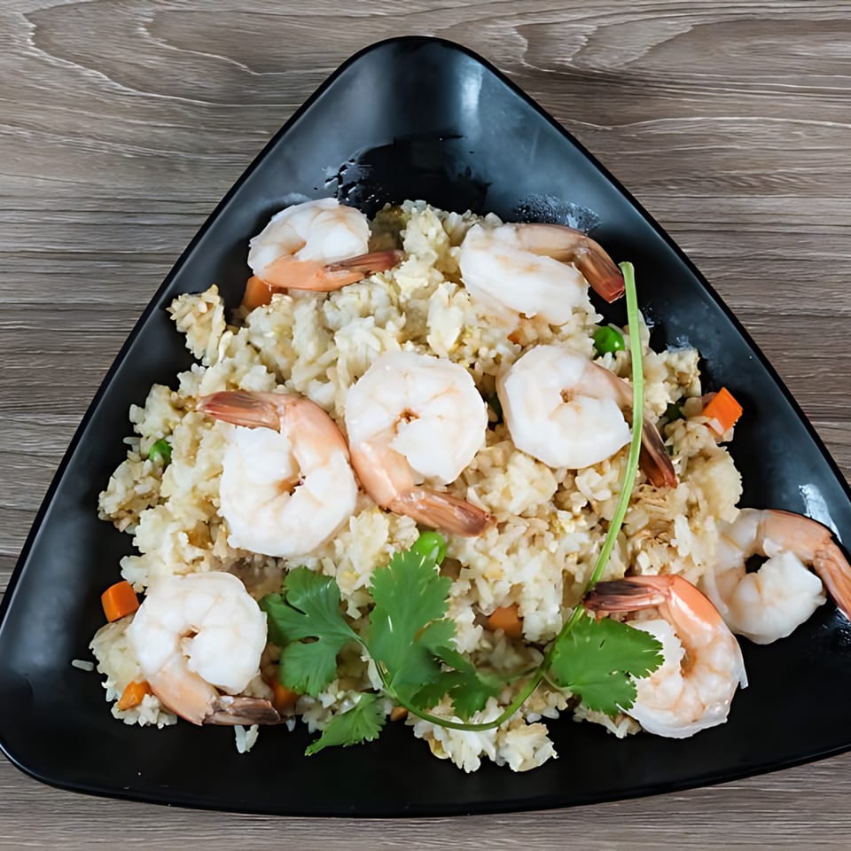 Shrimp fried rice with carrots, peas, and cilantro, served on a black triangular plate.