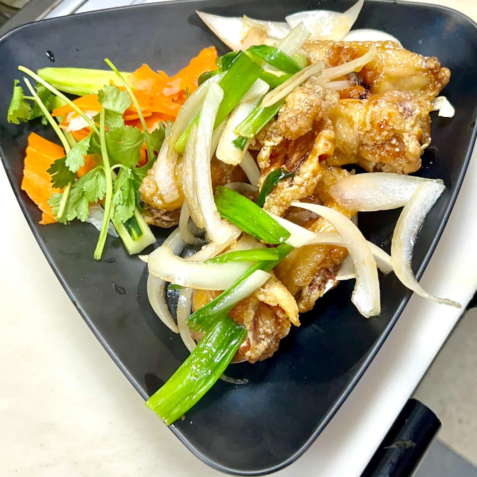 Crispy fried fish with sliced onions, green onions, carrots, and cilantro on a black plate.