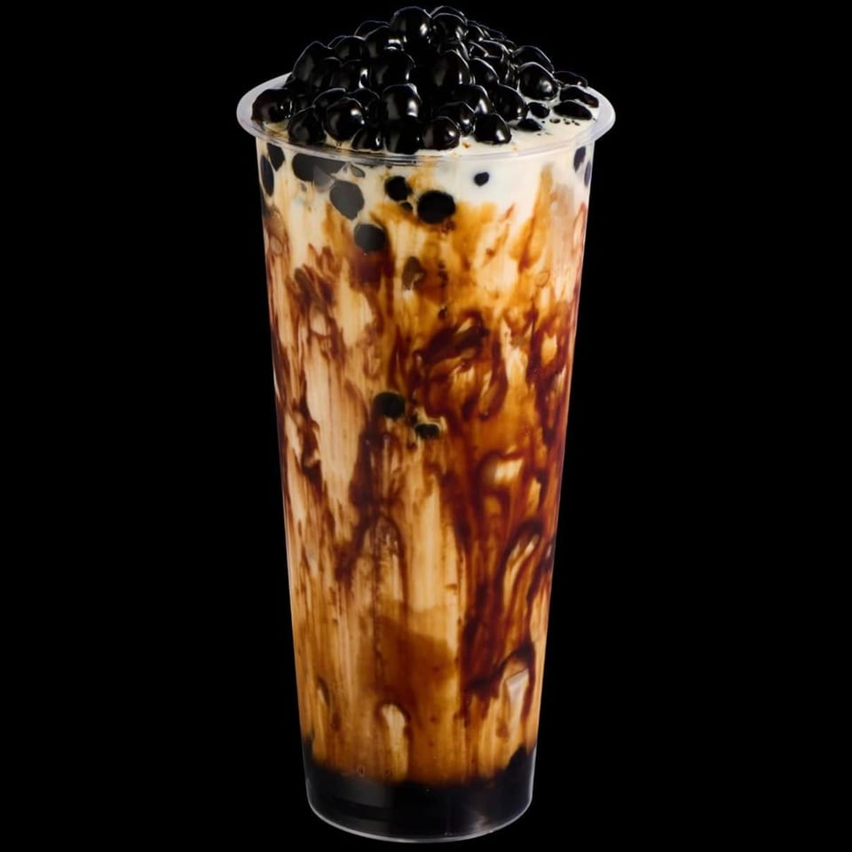 A tall plastic cup of brown sugar boba milk tea with dark pearls on top and swirling down the sides.