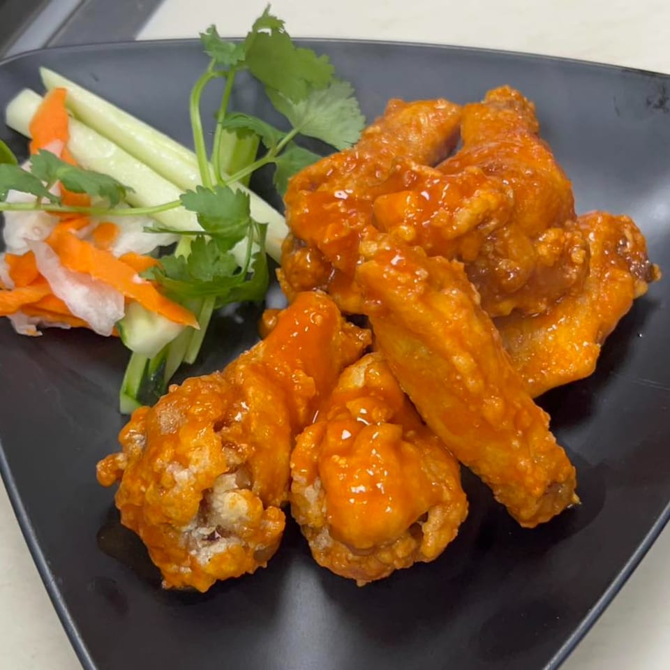 Sweet and sour chicken wings with pickled vegetables and cilantro on a black plate.