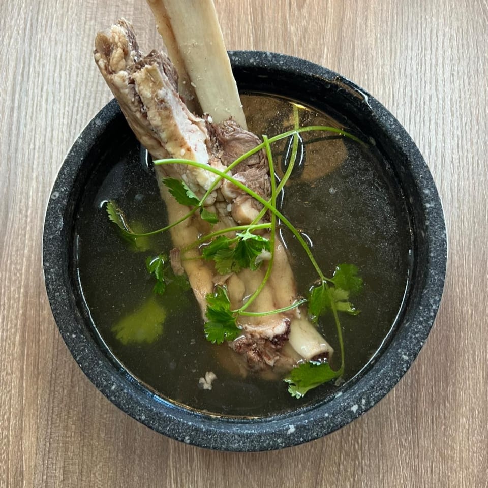 A large bone with meat and cilantro in a dark bowl of Pho Time pho broth.