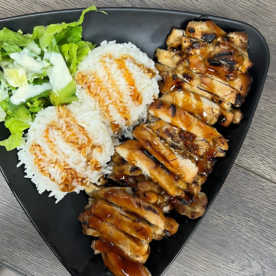 Teriyaki chicken with white rice drizzled with sauce, and a side salad on a black plate.