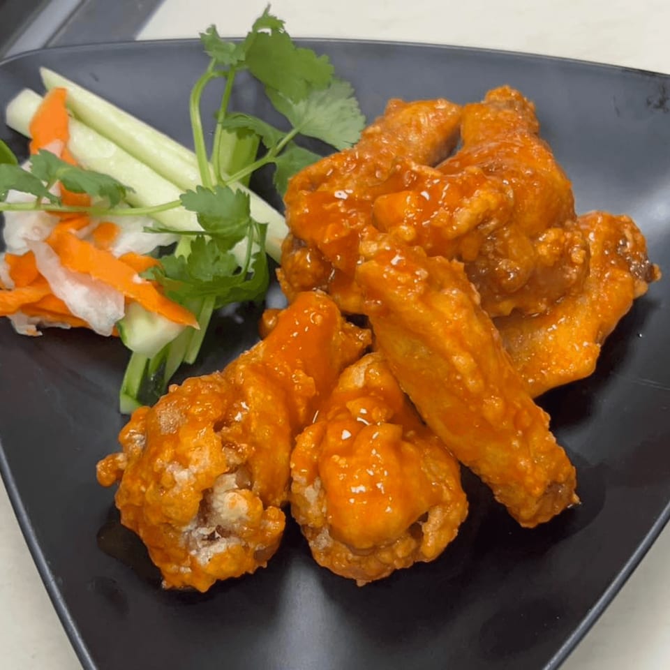 Sweet and sour chicken wings with pickled vegetables and cilantro on a black plate.